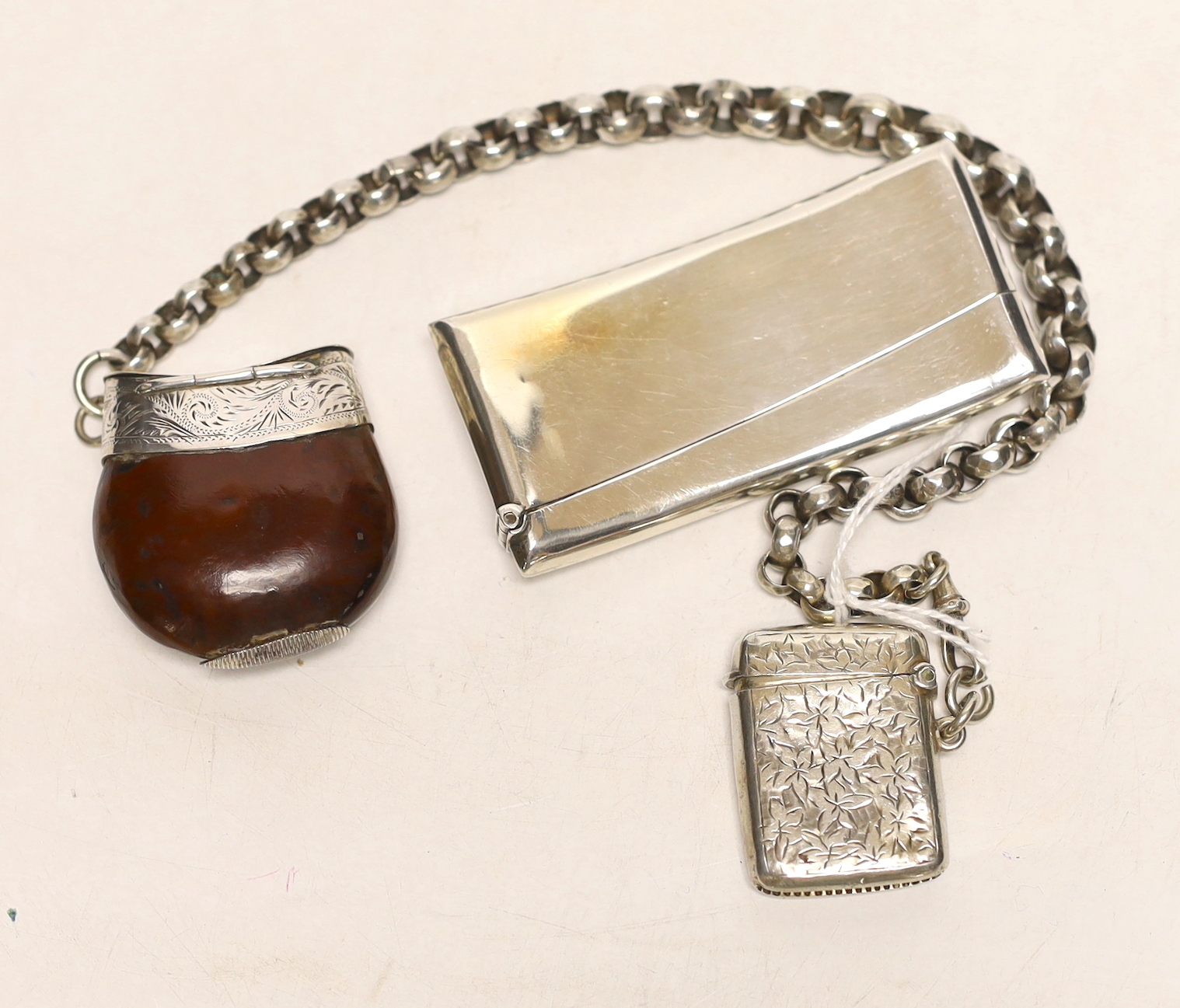 An Edwardian silver vesta case on a white metal belcher link chain, a 19th century white metal mounted nut vesta case and a George V silver card case, 83mm.